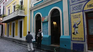Blue and yellow buildings on an Old San Juan street, with two men standing outside and chatting.