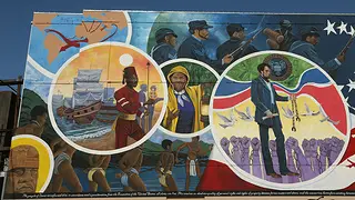 A detailed view of the mural Absolute Equality. This section depicts the transatlantic slave trade through a image of a globe, enslaved people shackled together in chains, Harriet Tubman, and Mustafa Zemmouri. 