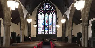 Interior of a church with red bows and stained glass at the back of the alter. 