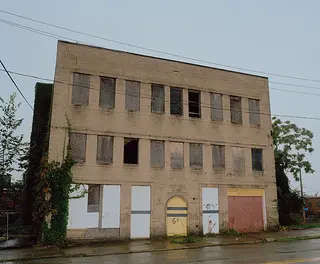 Exterior of a brick building with the ground floor windows and doors boarded up. 