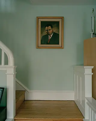 A portrait of Paul Robeson against a pale green wall with a set of stairs on the left hand side. 